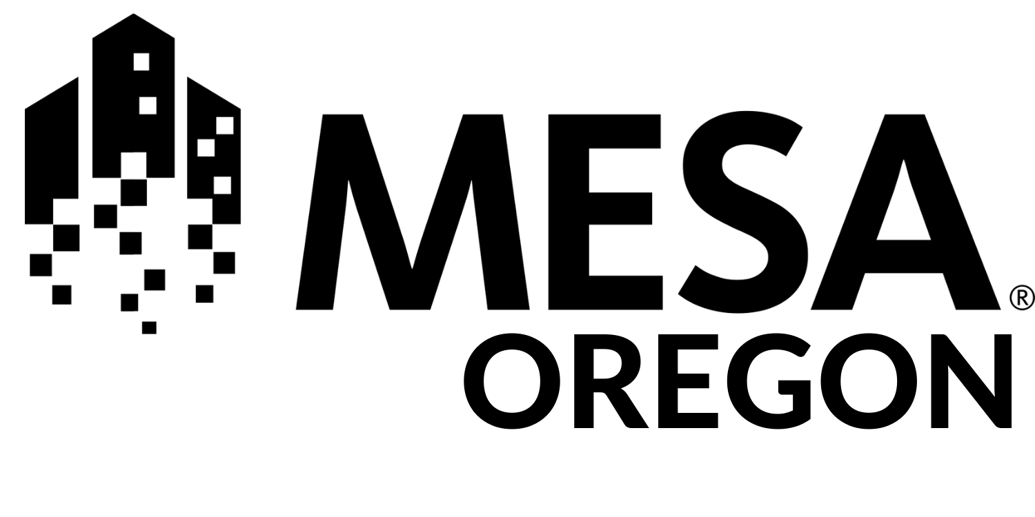 Oregon MESA Logo - black A person sits at a desk using a computer, surrounded by bookshelves filled with books. A cat sits on the desk, and a plant and a coffee mug are also nearby, creating a cozy workspace atmosphere.