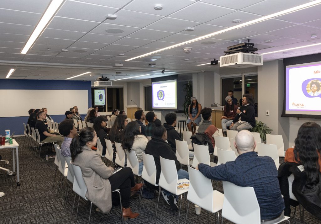 A group of people seated in a modern conference room listen to a panel discussion during Demo Day 2023. Presentation slides are displayed on screens, and four speakers face the audience in this photo gallery moment.