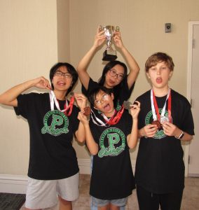 Four kids wearing black Chargers shirts pose indoors with medals around their necks. Smiling and making playful faces, these Oregon MESA students shine as one holds up a trophy after the 2025 National Engineering Design Competition.