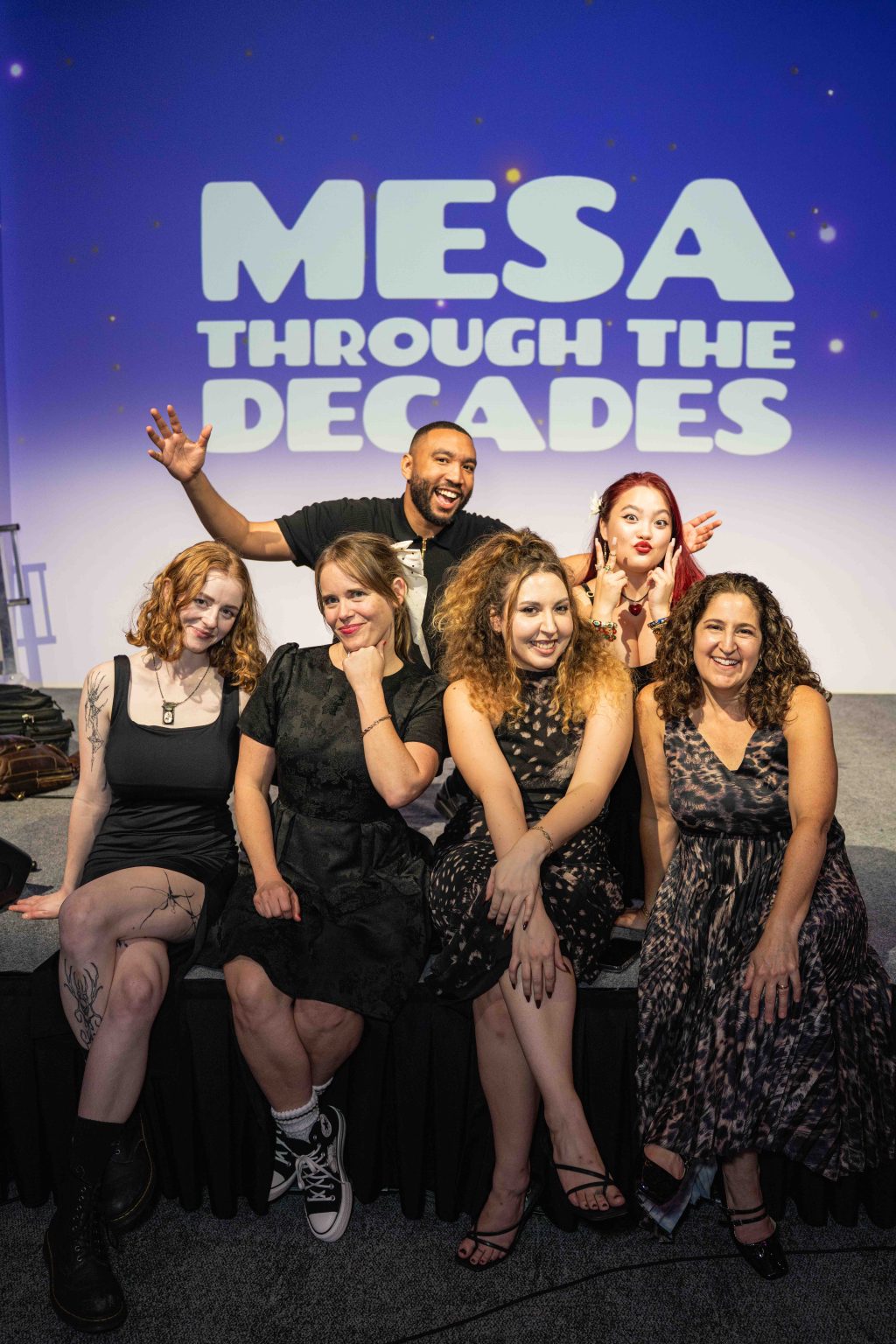 Six people pose and smile in front of a sign that reads MESA THROUGH THE DECADES. The group looks cheerful and celebratory, capturing a joyful moment for the MESA Through the Decades 2025 Photo Gallery.